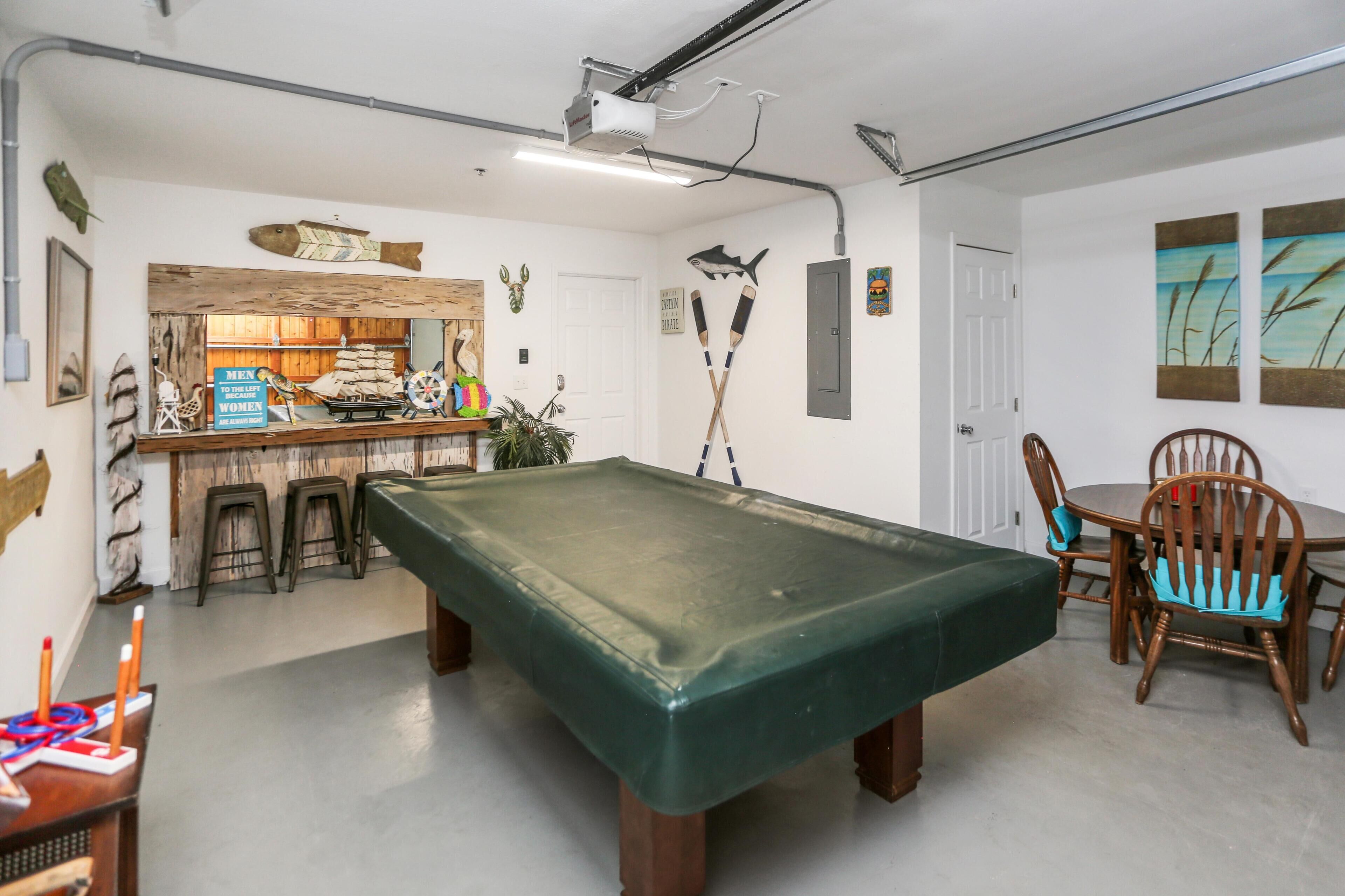 A pool table in a room with a bar area, wooden chairs, and various wall decorations including fish and a shark.
