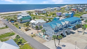 A coastal residential area with multiple two-story houses featuring blue roofs and balconies, situated near a beach with a clear view of the ocean.