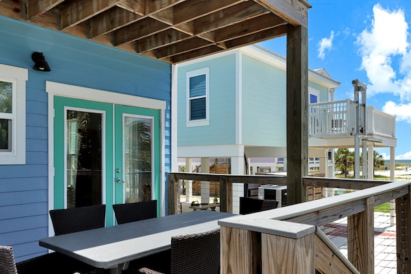 A covered outdoor seating area with a table and chairs, overlooking a beach and buildings. - Hesed Beach Cottage (Port St. Joe)
