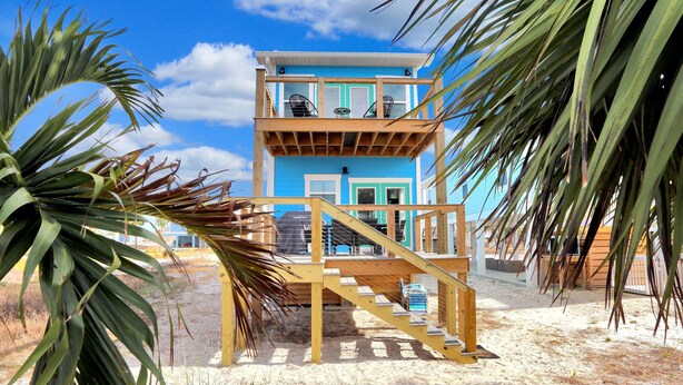 A two-story beach house with a wooden deck and a staircase leading to the upper level. - Hesed Beach Cottage (Port St. Joe)