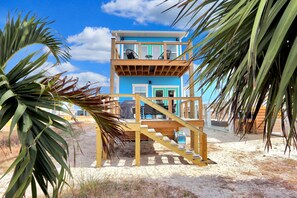 A two-story beach house with a wooden deck and a staircase leading to the upper level. - Hesed Beach Cottage (Port St. Joe)
