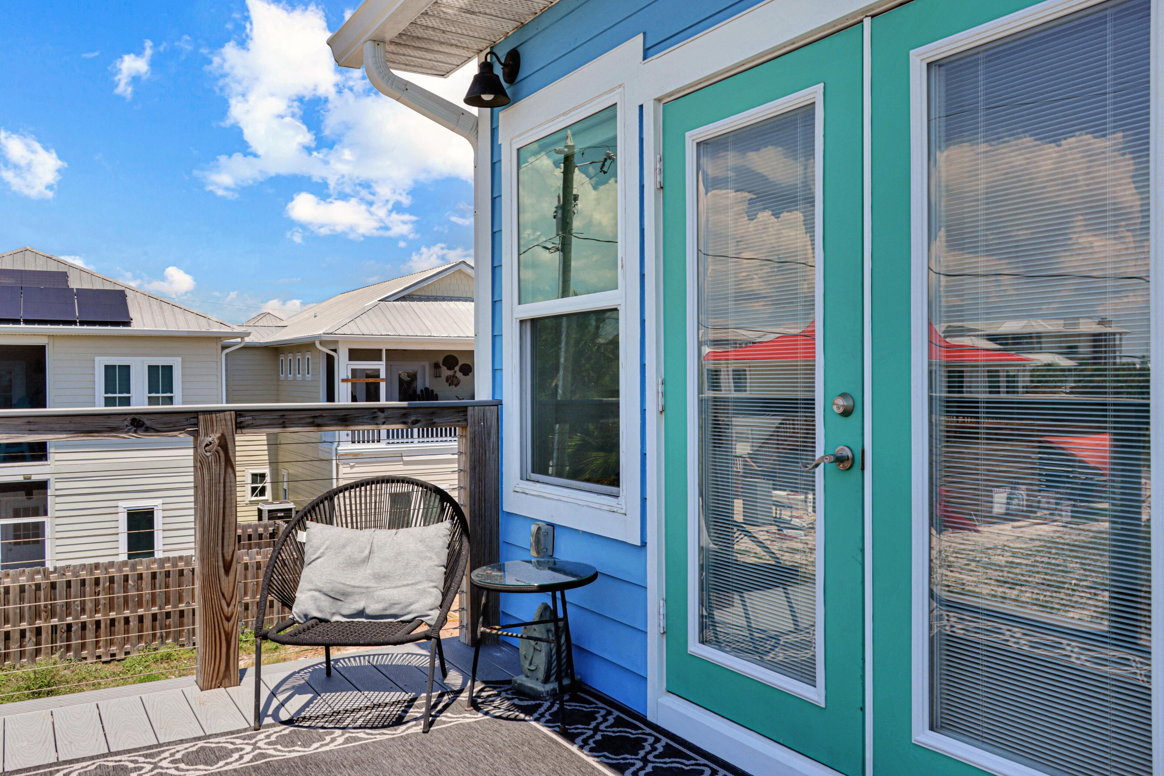 A covered patio with a chair and table, a door with a screen, and a view of neighboring houses.