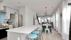 A modern kitchen with a central island, bar stools, and a dining area with a table and chairs. - Hesed Beach Cottage (Port St. Joe)