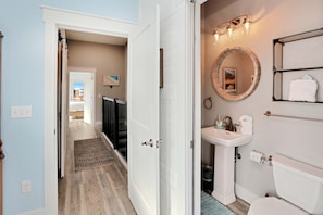 A hallway leading to a bathroom with a sink, toilet, and a mirror. - Hesed Beach Cottage (Port St. Joe)