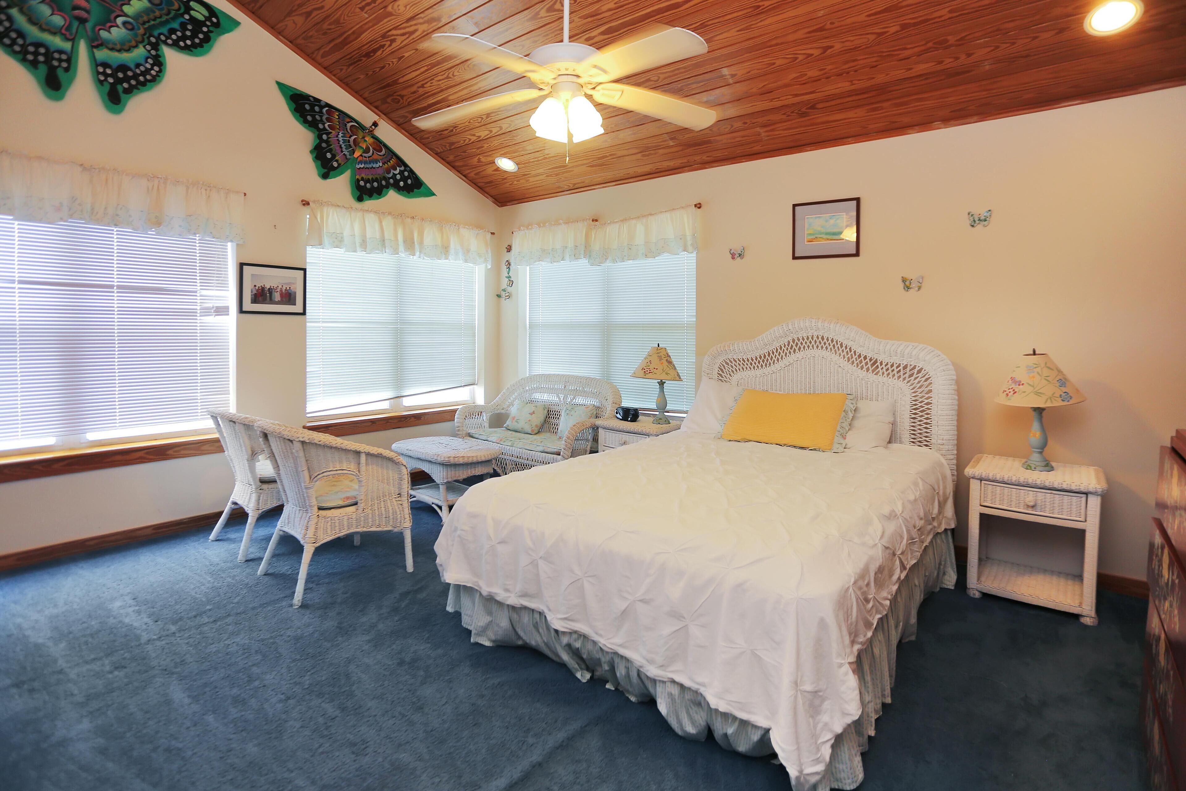 Ein Schlafzimmer mit einem Bett, einem Sessel, einem Nachttisch und einem Deckenventilator.