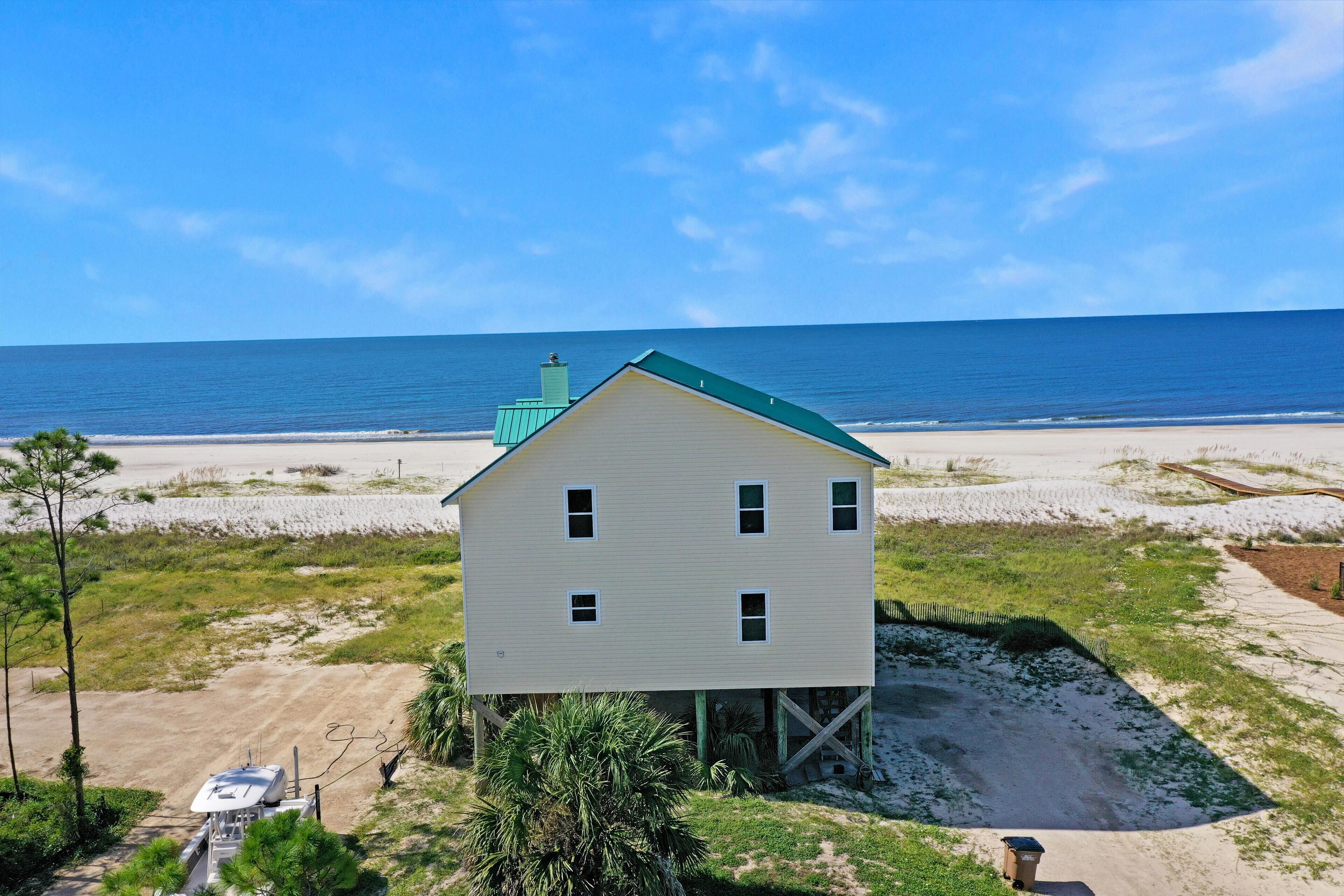 A two-story house with a green roof, located on a sandy beach with a view of the ocean.