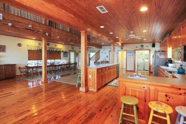 A spacious kitchen with wooden cabinets, a central island with stools, and a dining area with chairs and a table.