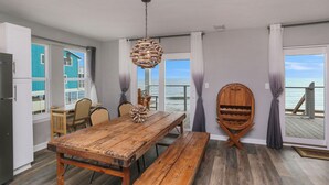 Una cocina amplia con una mesa y banco de madera, una lámpara colgante y vistas al océano a través de amplios ventanales.