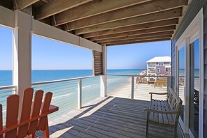 Une terrasse en bois avec un banc, donnant sur une plage, avec une maison en arrière-plan.