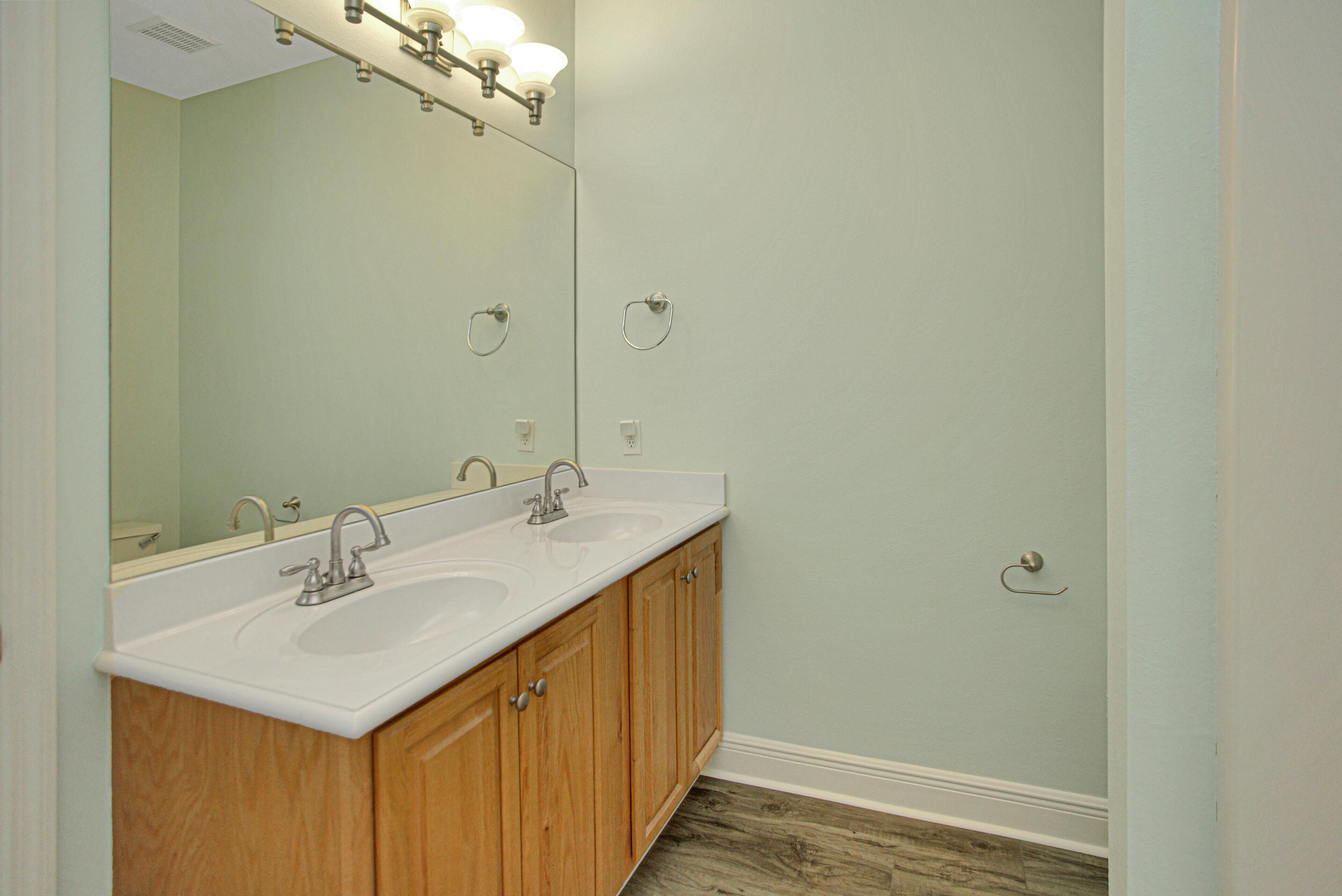 A bathroom with two sinks, wooden cabinets, a large mirror, and a light fixture above the mirror.
