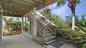 Eine Holztreppe führt zu einem überdachten Bereich mit Betonboden und einer Palme im Hintergrund.