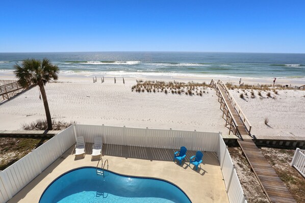 A beach view with a pool, lounge chairs, and a wooden deck.
