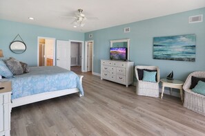 A bedroom with a bed, dresser, chairs, a TV, and artwork on the wall.