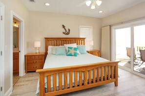 A bedroom with a wooden bed, two bedside tables with lamps, a large window, and a view of the outdoors.