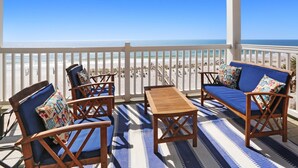 Een balkon met houten meubels, een gestreept tapijt en uitzicht op het strand.