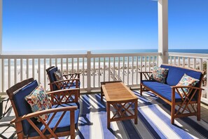 A balcony with wooden furniture, a striped rug, and a view of the beach.