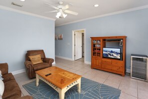 A living room with a brown leather chair, a wooden coffee table, a television on a wooden cabinet, and a ceiling fan. - Five on the Beach (Port St. Joe)