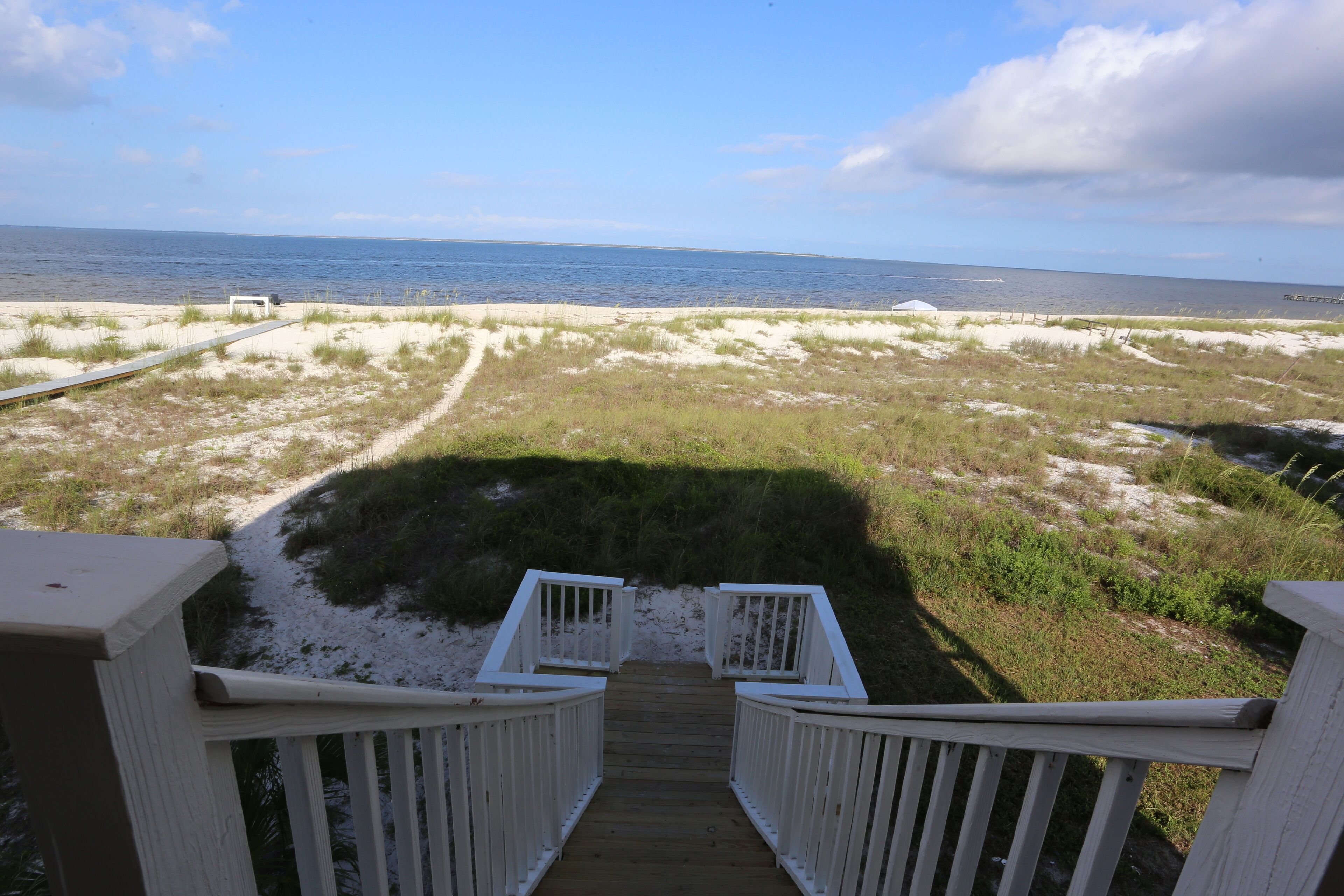 A wooden deck leading to a sandy beach with a clear view of the ocean.