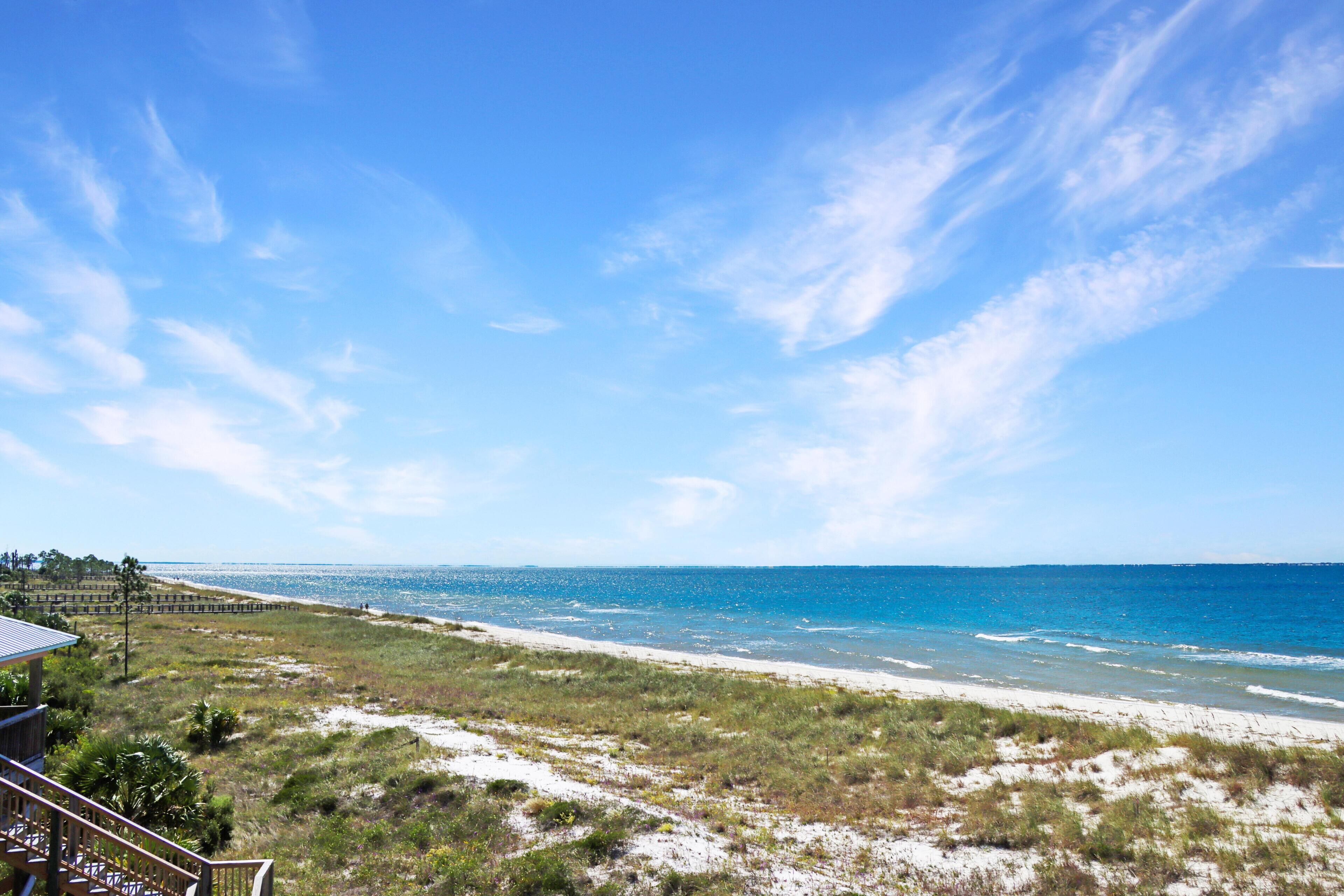 A beach view with a wooden deck and a clear sky.