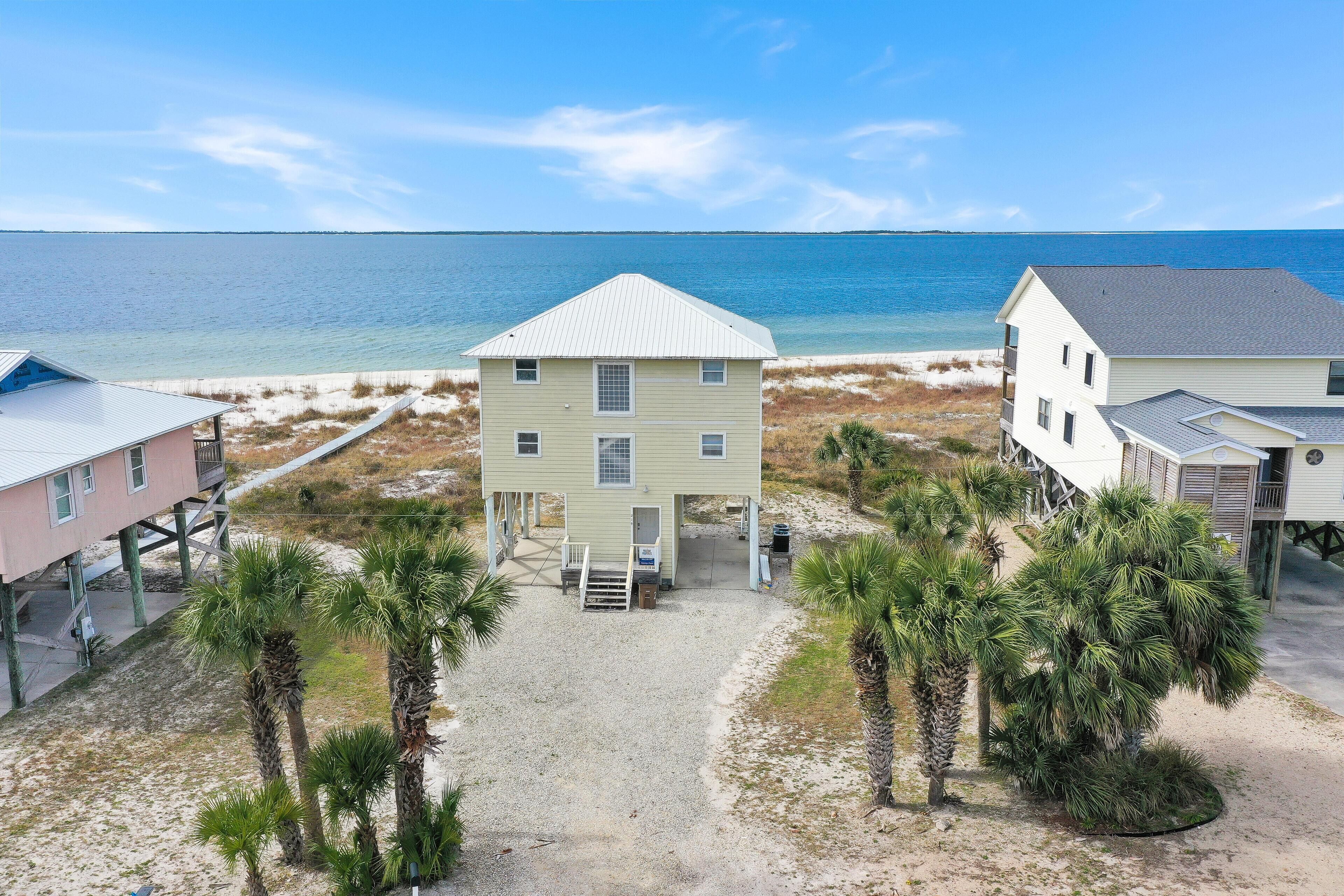 A beachfront property with a central house, two smaller buildings, and palm trees.