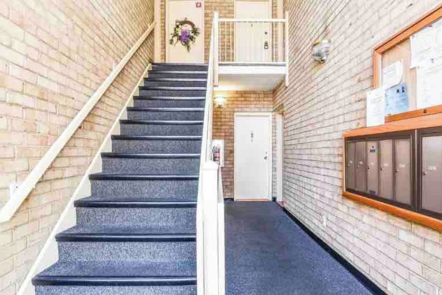 A staircase leading to a door with a wreath, a small balcony, and a row of lockers on the right.
