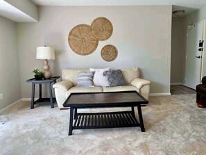 A living room with a sofa, a coffee table, a lamp, and wall art.