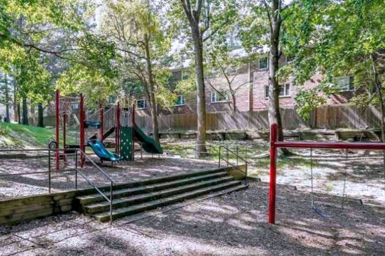 A playground with a slide and climbing structures, surrounded by trees and a wooden fence.