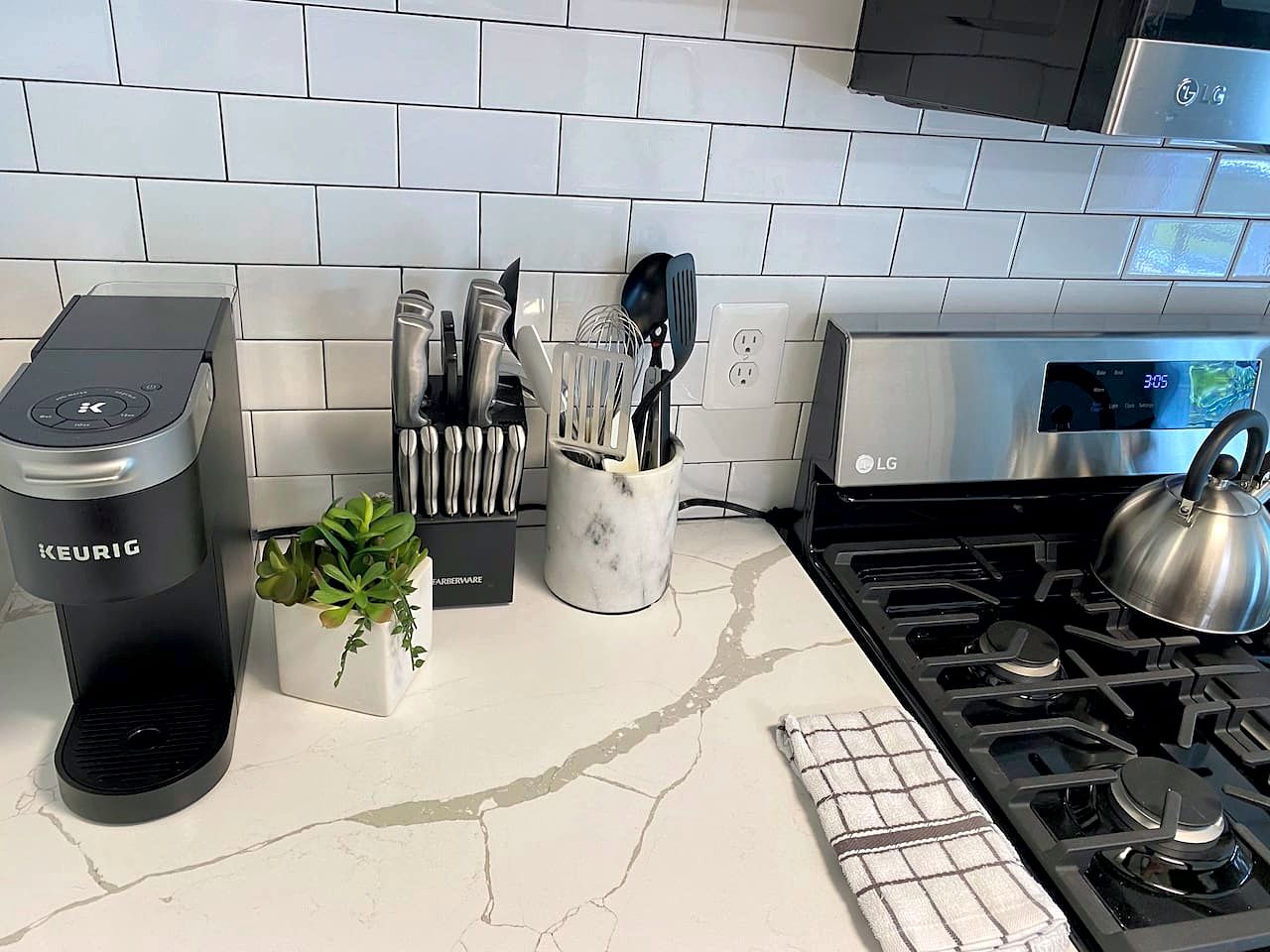 A kitchen with a Keurig coffee maker, a marble countertop, a gas stove, and a backsplash.