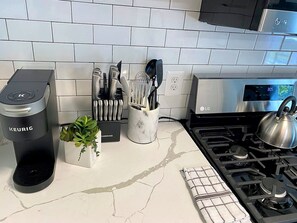 A kitchen with a Keurig coffee maker, a marble countertop, a gas stove, and a backsplash.