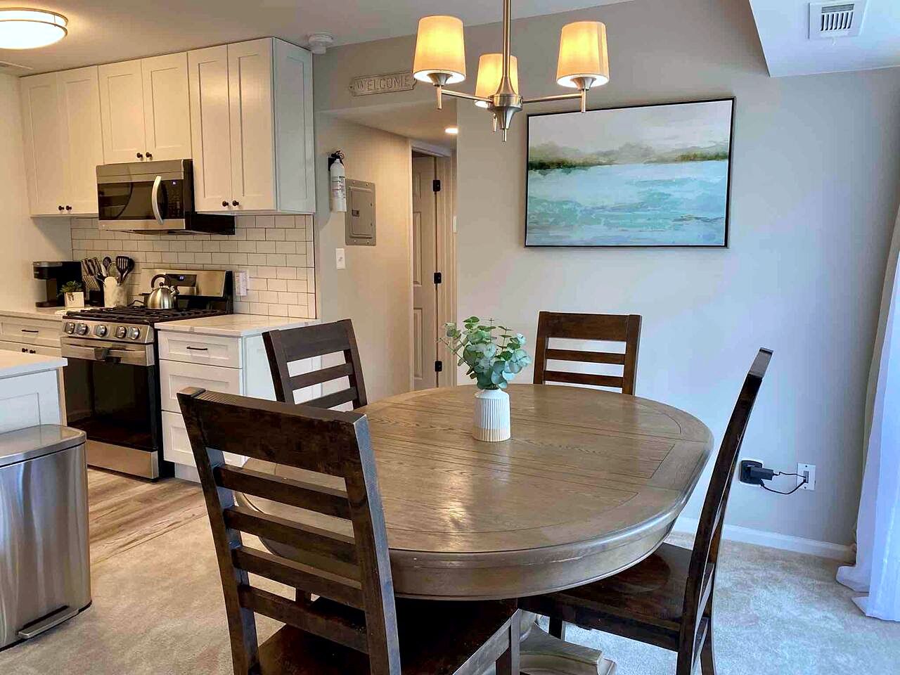 A kitchen with white cabinets, a microwave, stove, and a dining area with a round table and chairs.