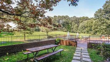 A picnic area with a wooden bench and picnic table, surrounded by a brick wall and a metal fence.