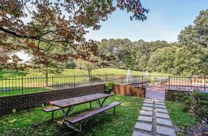 Et picnicområde med træbænk og picnicbord, omgivet af en murstensmur og et metalhegn.