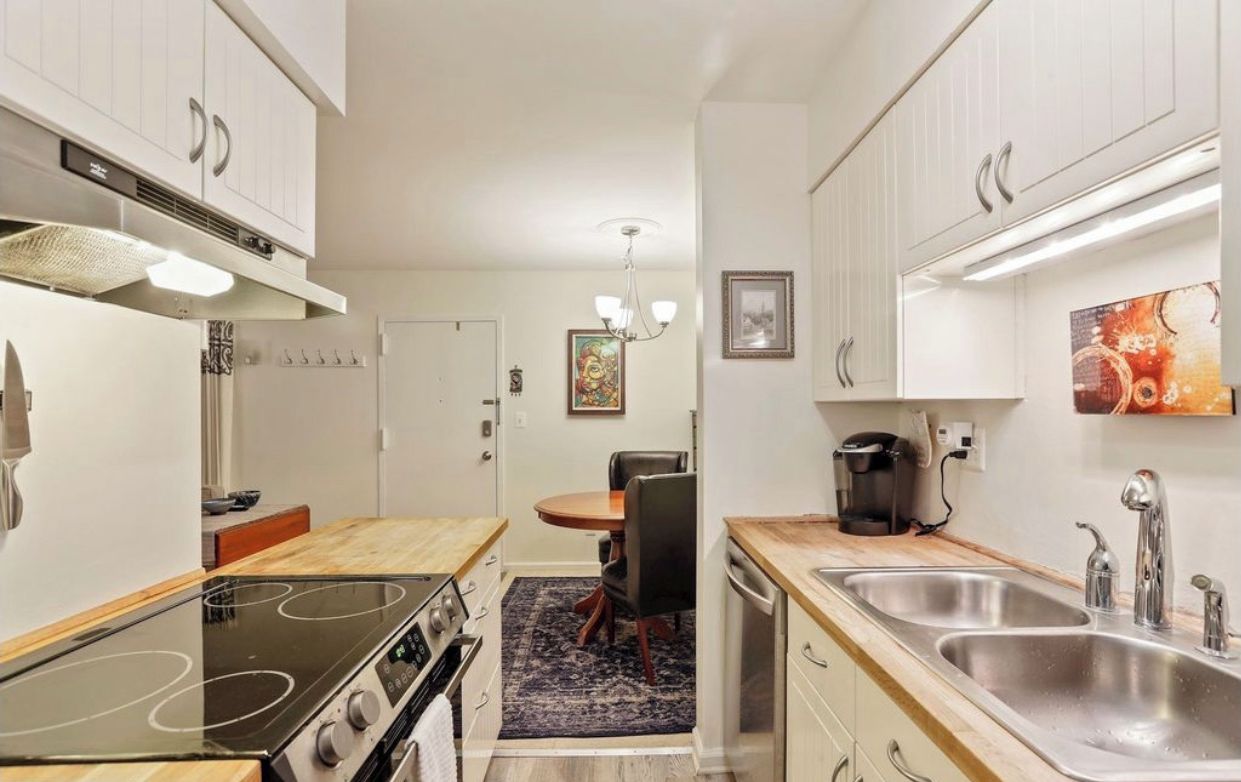 A compact kitchen with white cabinets, a stove, a sink, and a dining area with a table and chairs.