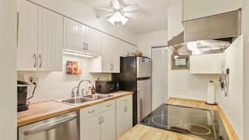 A compact kitchen with white cabinets, a stainless steel refrigerator, a microwave, and a sink.