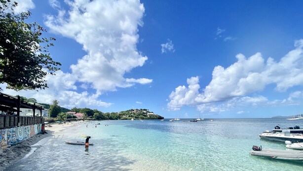 A beach with clear turquoise water, boats, and a building with a mural. - Beau T3 vue mer Proche Plage Wifi (Trois Ilets)