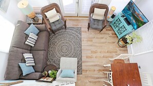 Un salon moderne avec un canapé gris, deux fauteuils, une table basse, une table à manger en bois et un grand téléviseur.