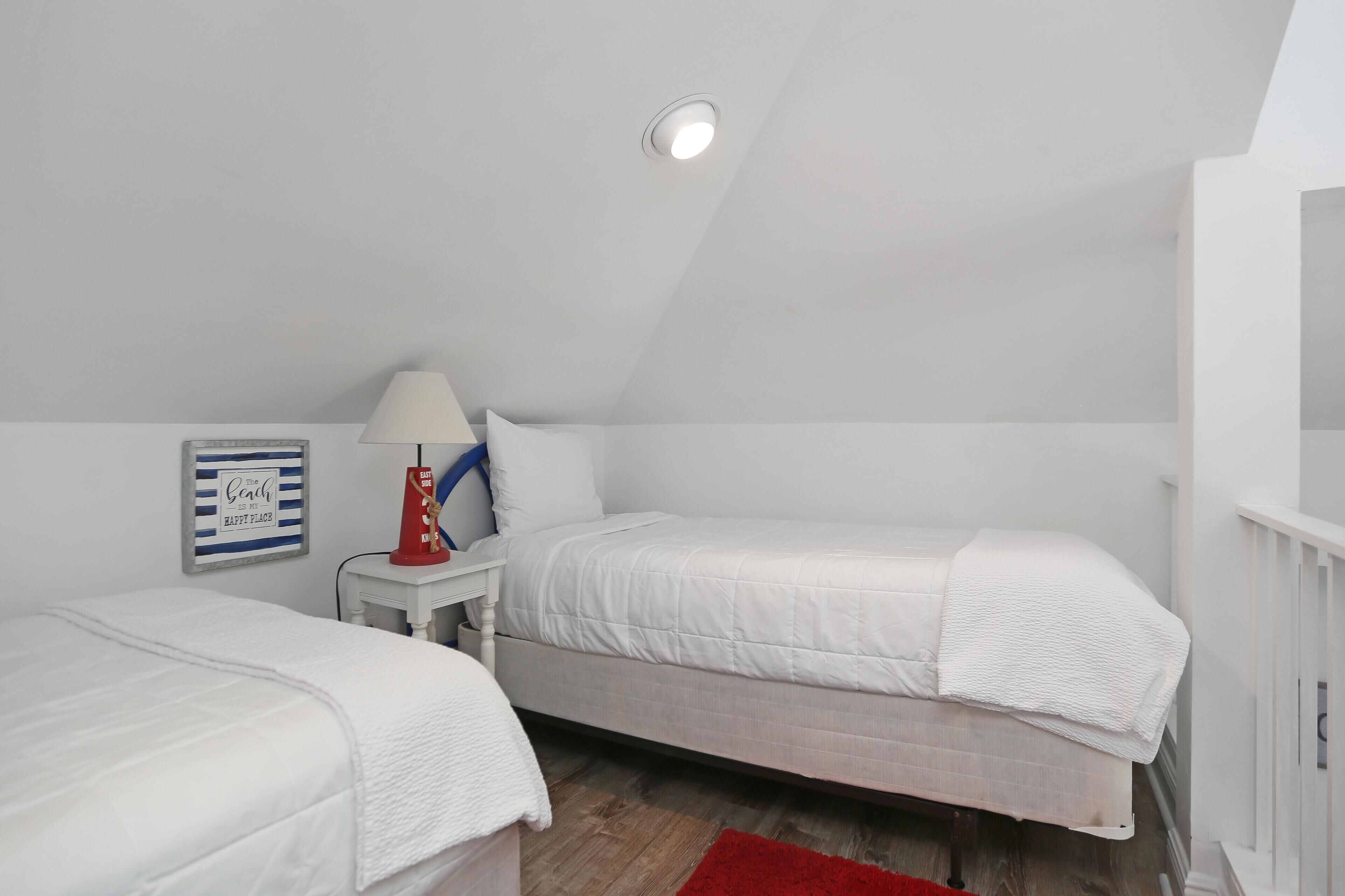A bedroom with two single beds, a red lamp, a white nightstand, and a ceiling light.