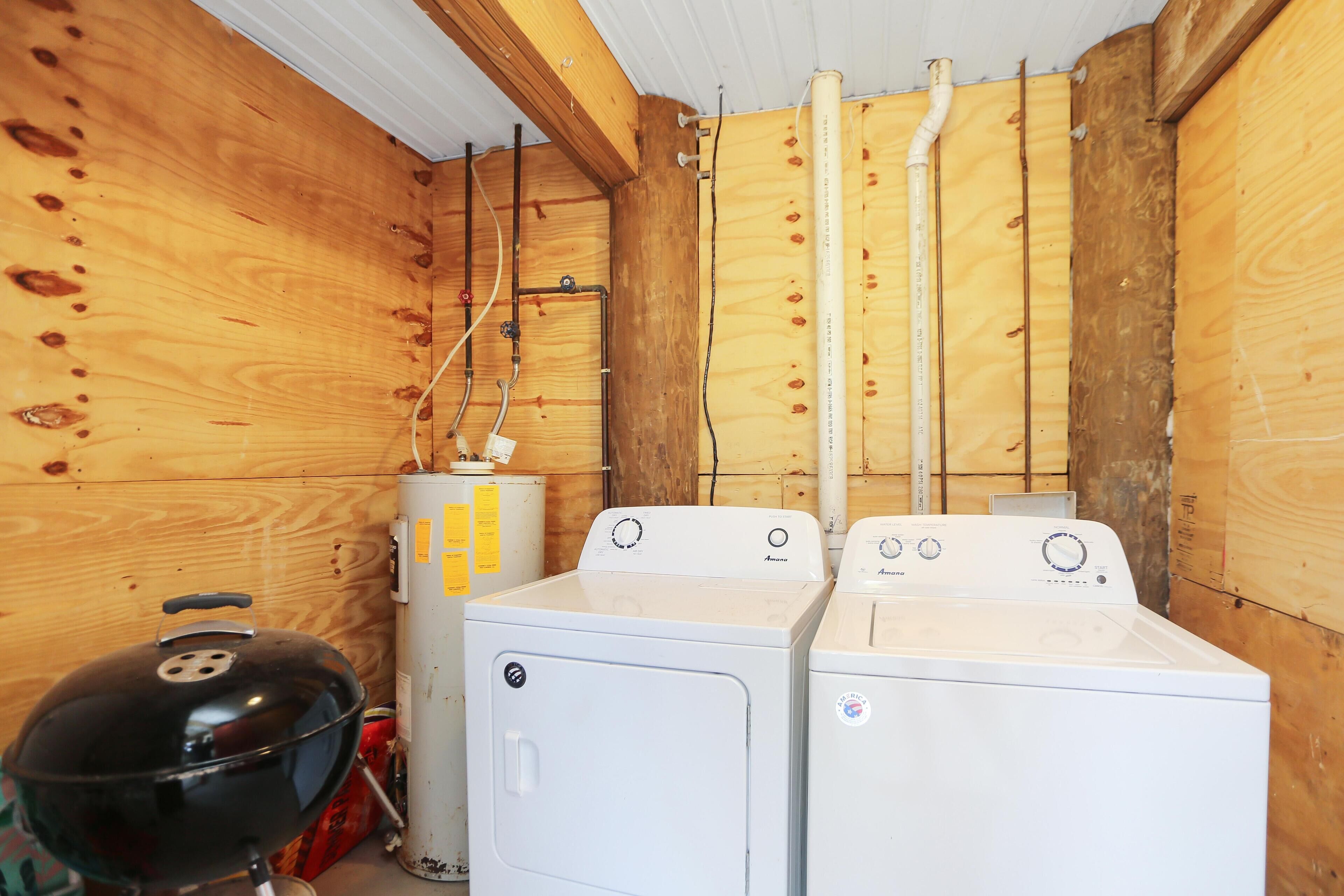 A laundry room with two white washing machines, a barbecue grill, and wooden walls.