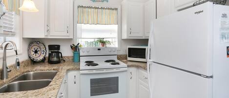 Une cuisine avec des meubles blancs, une cuisinière, un évier, un four à micro-ondes et un réfrigérateur.