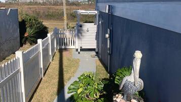 A narrow pathway leading to a house with a white picket fence, a wooden barrel with seashells, and a potted plant.