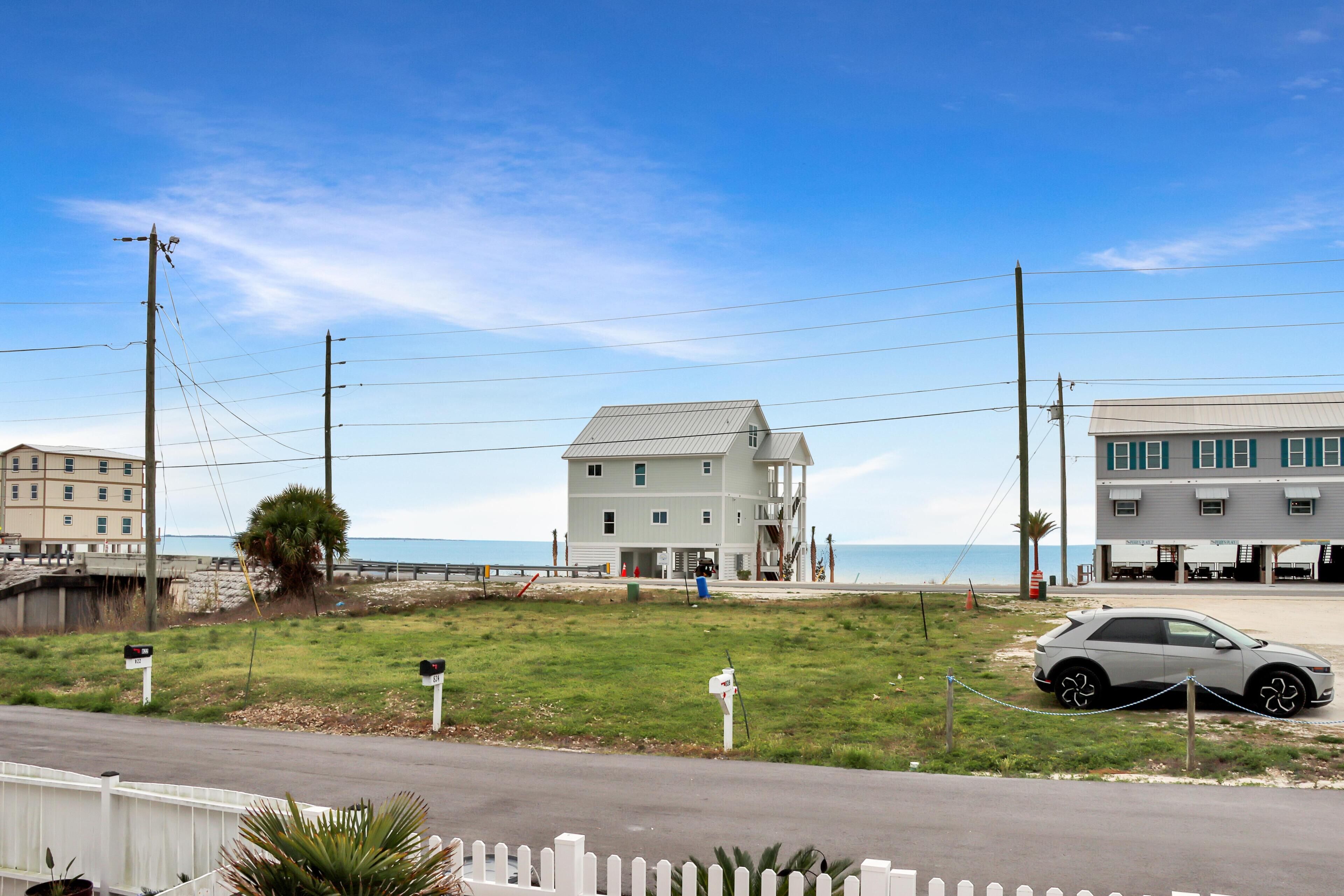 A beachfront property with a large white building, a smaller adjacent structure, and a parked car.