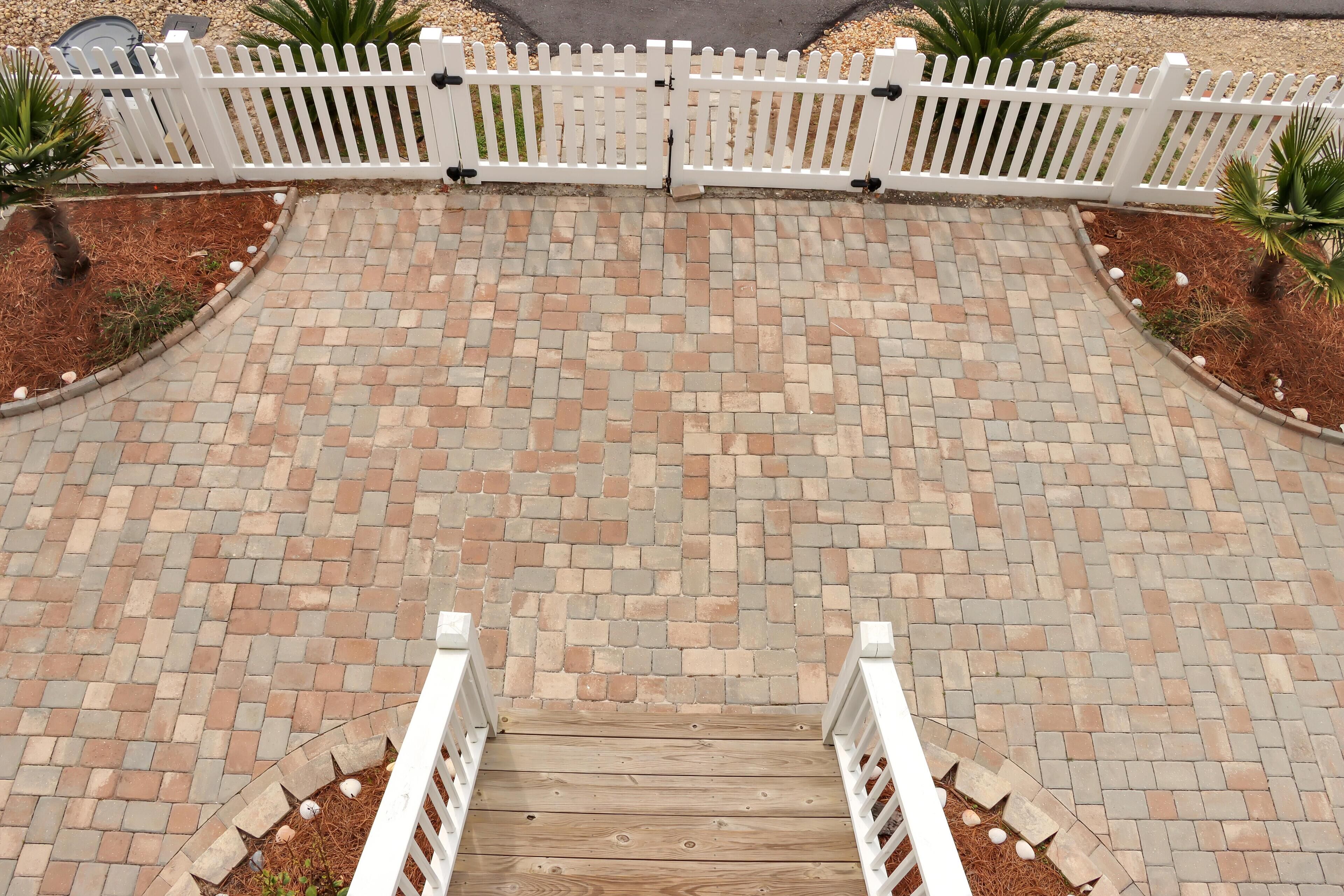 A brick pathway leading to a white picket fence.