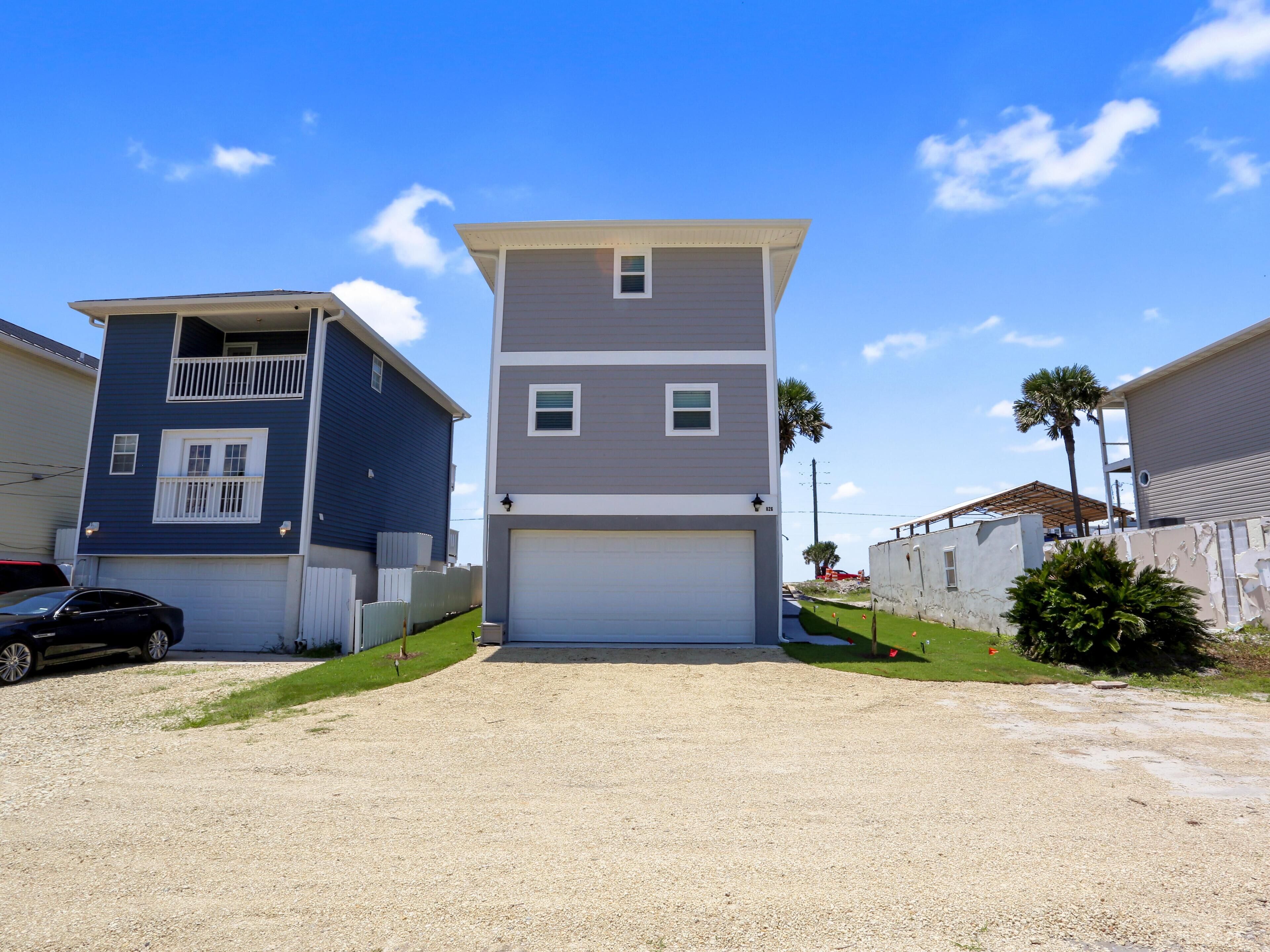 A two-story residential building with a garage, a balcony on the upper floor, and a gravel driveway.