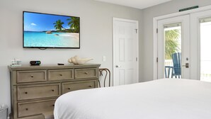 Een slaapkamer met een bed, een dressoir, een televisie waarop een strandafbeelding staat en een deur naar een balkon.