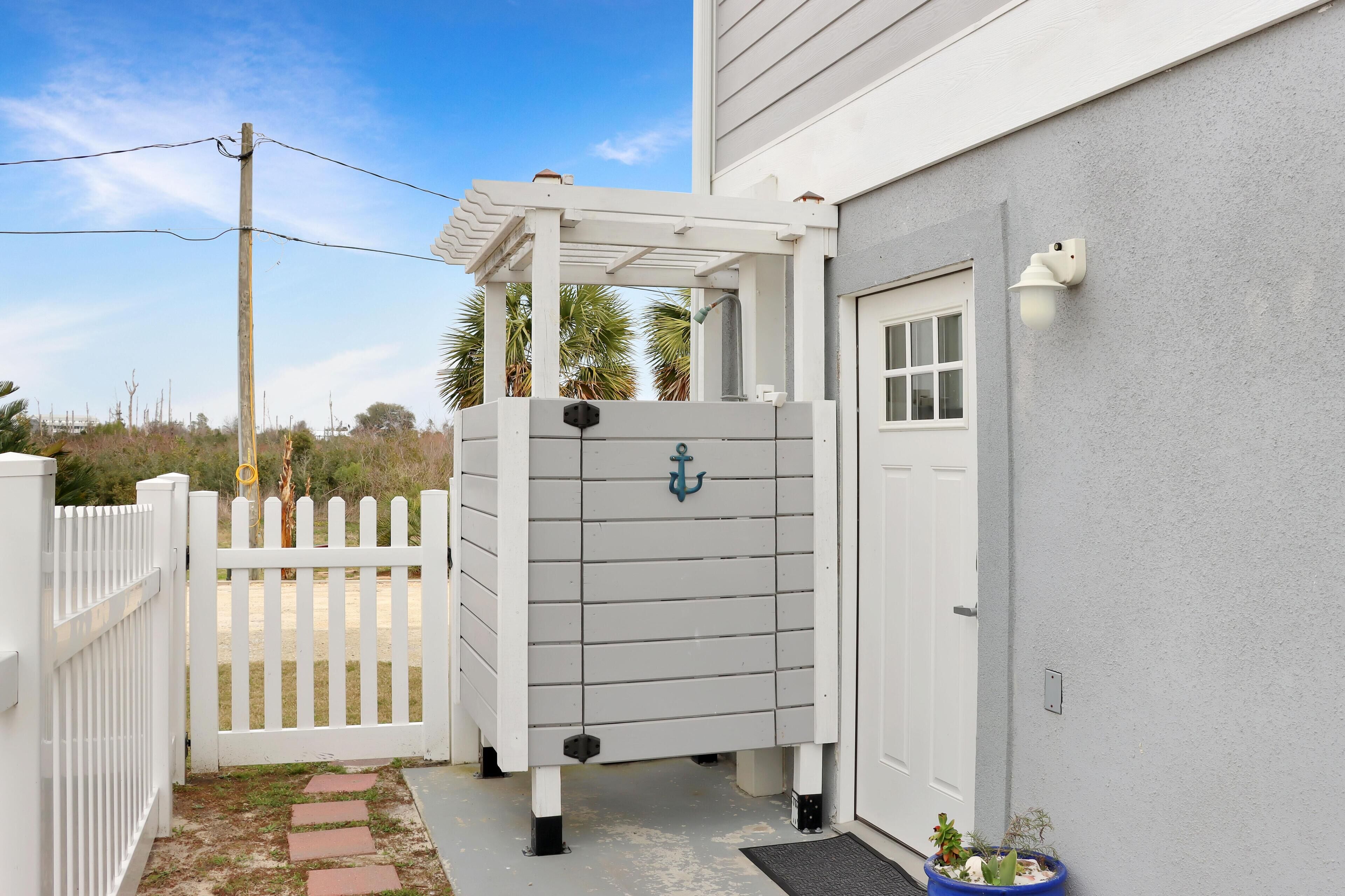 A white wooden structure with an anchor symbol, a white picket fence, and a door with a window.