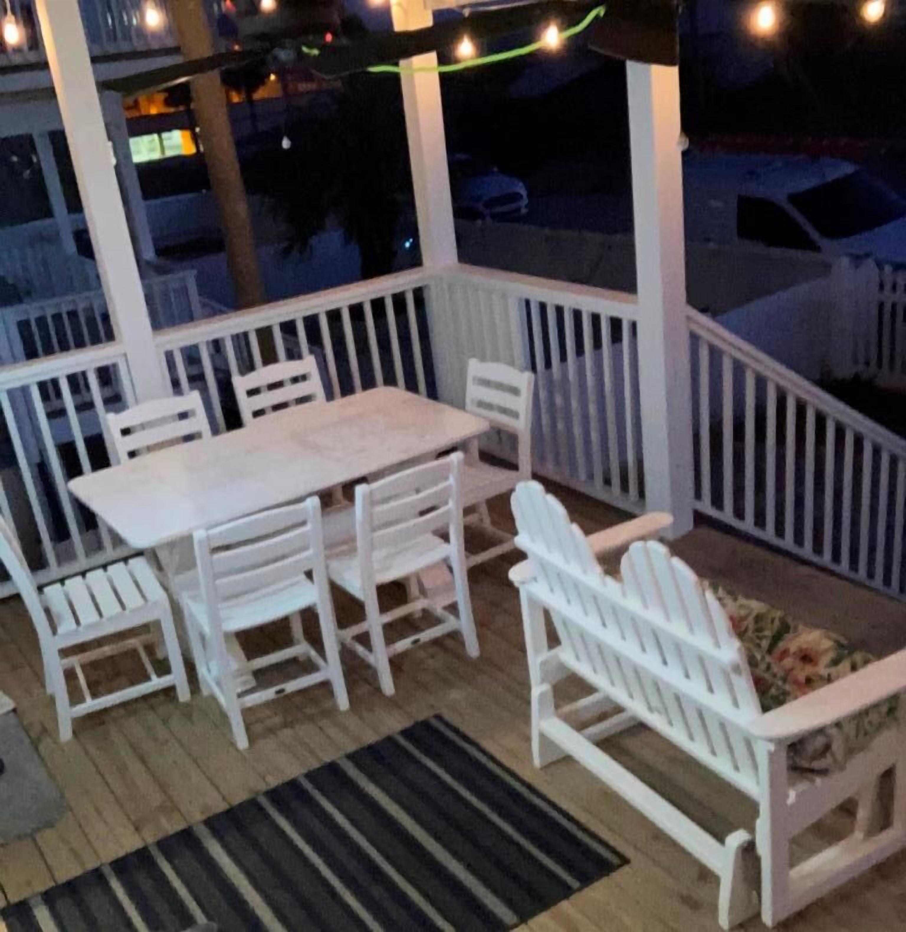 A covered outdoor seating area with a table and chairs, a bench, and string lights.