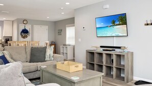 Een moderne woonkamer met een beige bank, een bijzettafeltje en een televisie waarop een strand te zien is.