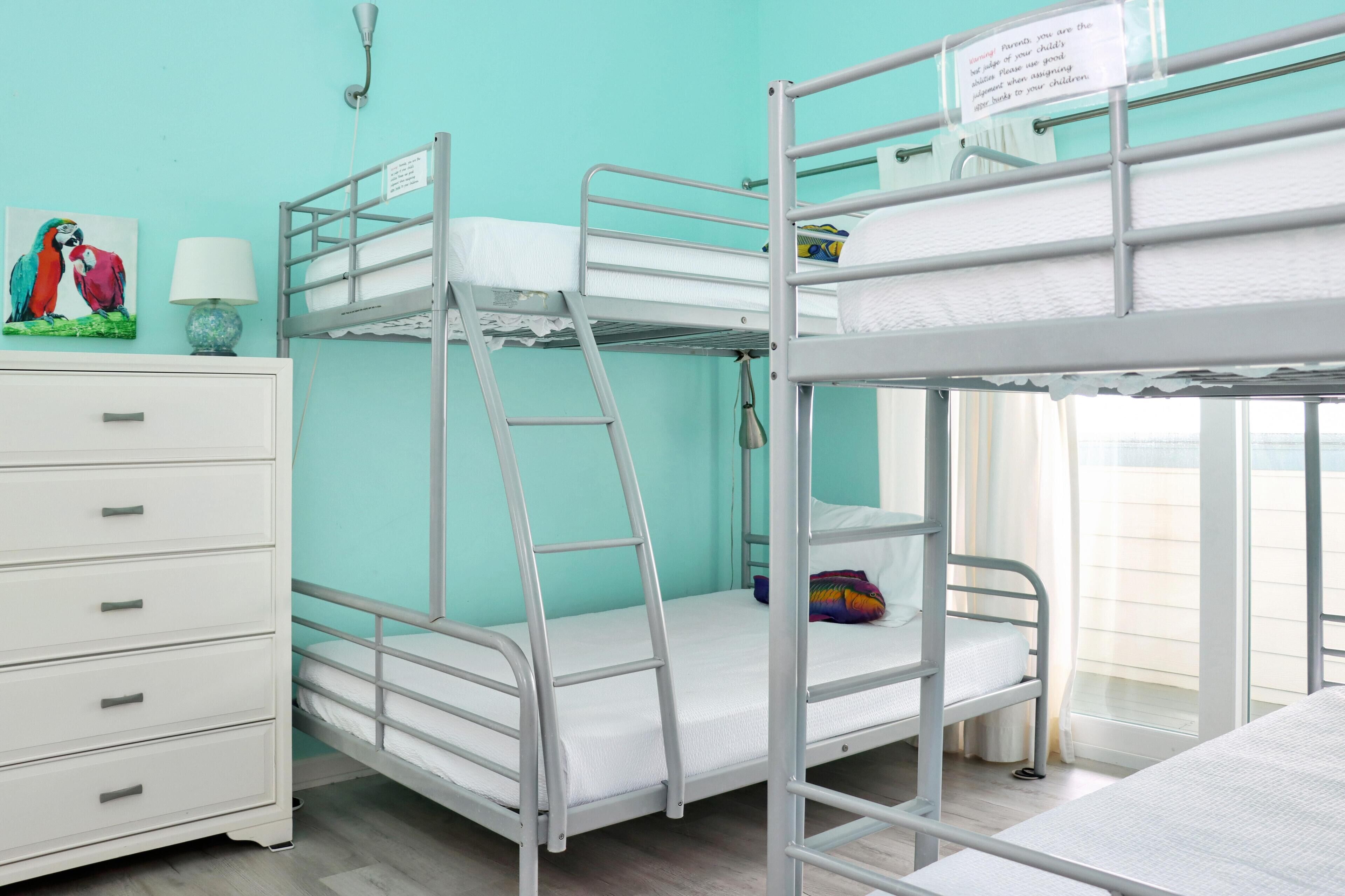 Habitación con literas, un aparador blanco, una lámpara y un cuadro de un loro.