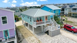 Une propriété située en bord de mer, avec une maison à deux étages dotée d’un balcon, d’une terrasse couverte et d’un SUV rouge garé devant.