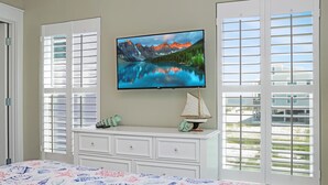 Une chambre à coucher avec un lit, un téléviseur fixé au mur, une commode et une fenêtre avec des stores.